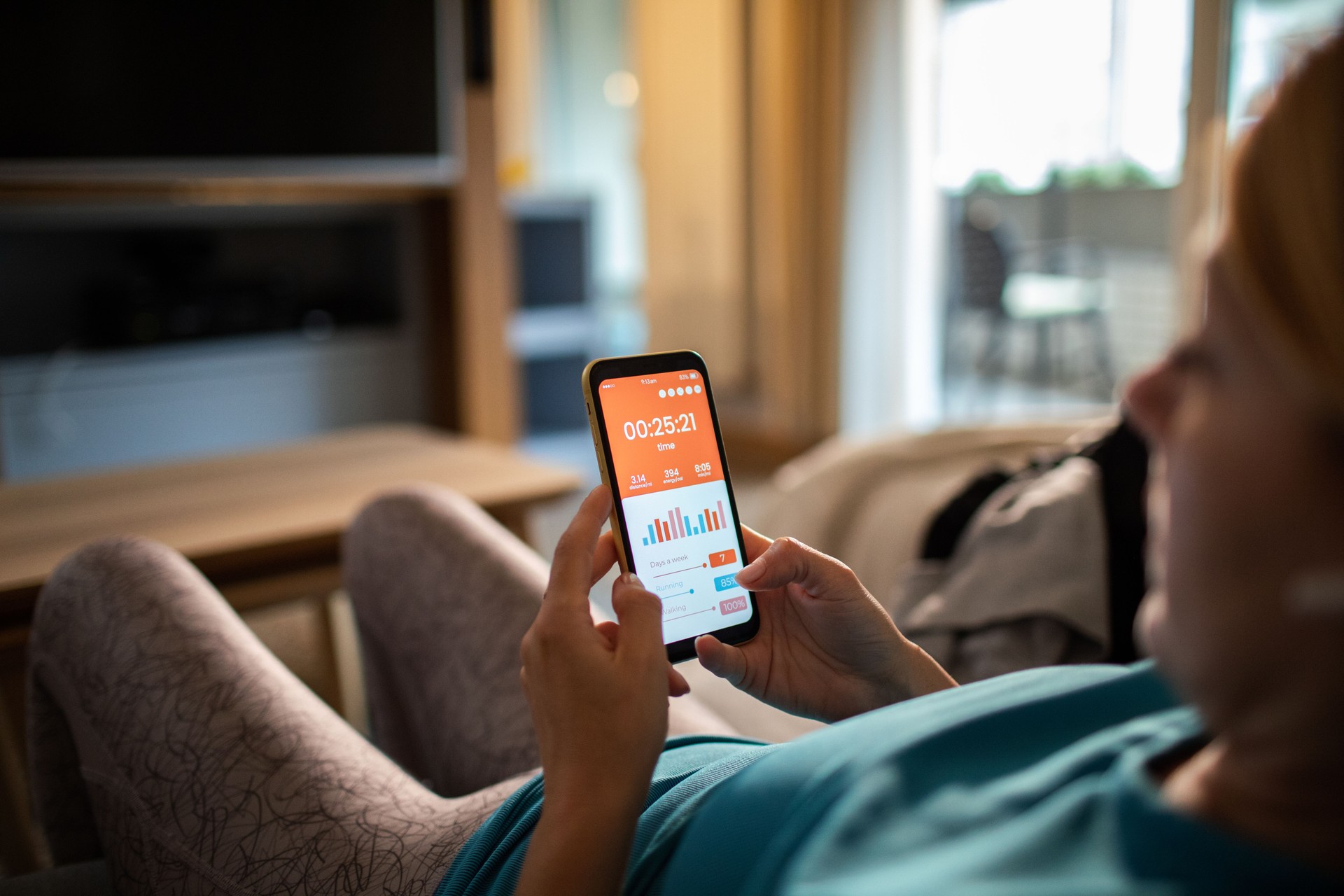 Young adult woman using a fitness app on her smart phone at home